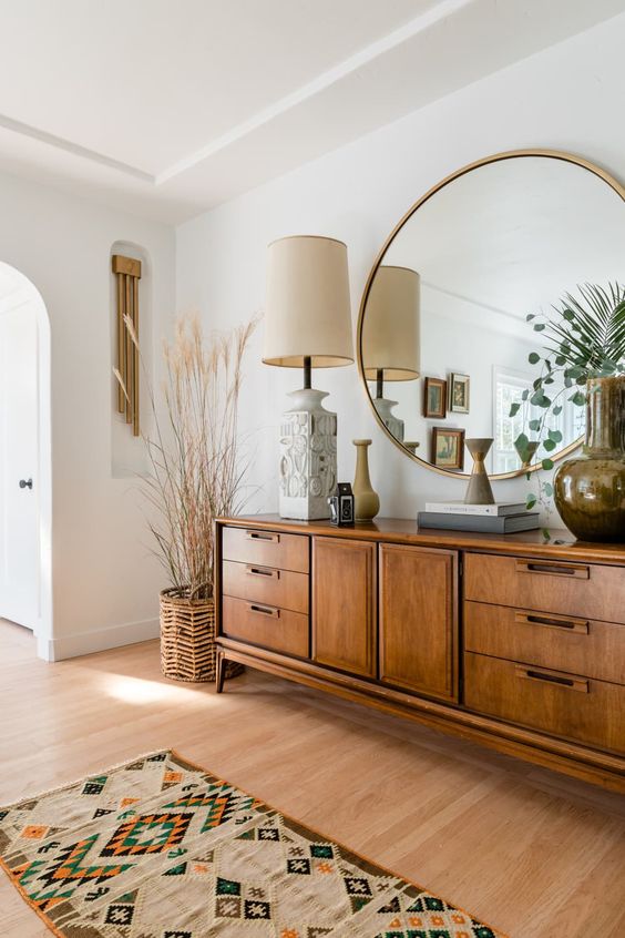 a chic mid-century modern space wiht a stained credenza, a round mirror, some vases and a table lamp plus a printed boho rug