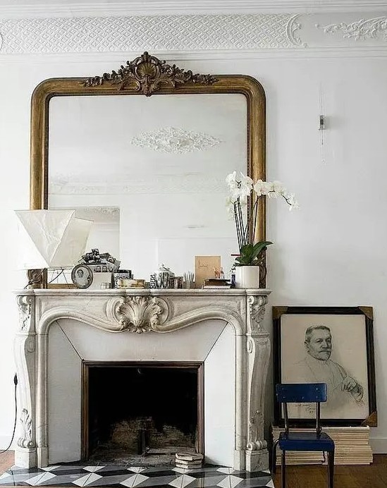 a chic vintage French fireplace with an ornated mantel, some pretty mantel decor, an oversized mirror and some books