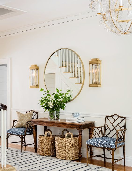 a cihc entryway with a vintage stained table, antique chairs, a round mirror in a gold frame and vintage sconces