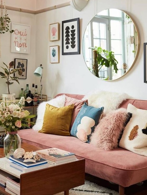a colorful eclectic living room with a pink sofa, colorful pillows, potted plants, a gallery wall and a round mirror