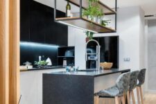 a contemporary black and white kitchen with built-in lights, a kitchen island with a waterfall countertop and a suspended shelf