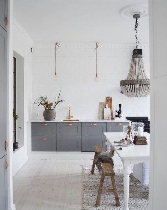 a contemporary meets vintage kitchen with grey cabinets, pendant lamps and a chandelier, a white vintage table and benches