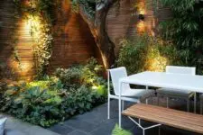 a contemporary townhouse garden with stone tiles, minimalist furniture of wood and metal, lush textural greenery and a tree growing