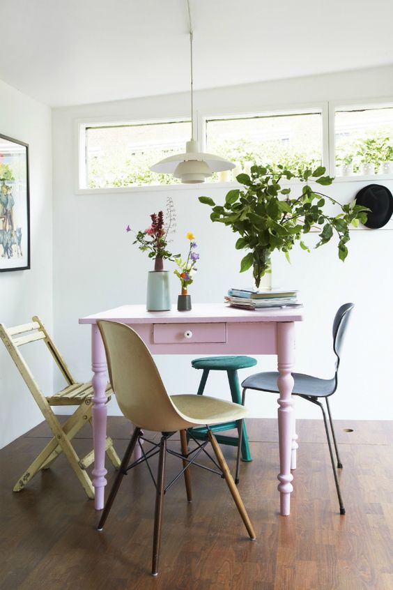 a cool dining space with a pink vintage table, mismatching pastel chairs, a pendant lamp and greenery is all cool