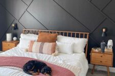 a cozy bedroom with a black geo accent wall, a stained bed and nightstands, white and pink bedding, a woven pendant lamp