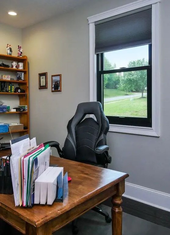 a cozy farmhouse home office with a black frame double-hung window, a stained desk and a bookshelf, some books and decor