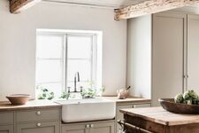 a cozy farmhouse neutral kitchen with grey cbainets, wooden countertops and beams, a wooden cart kitchen island