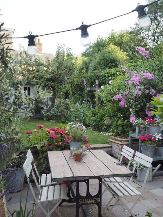 a cozy little garden with a green lawn, greenery and trees, some potted blooms is a cool space to spend some time, and a dining space makes it even better