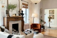 a cozy living room with a French fireplace with a refined stained mantel, neutral seating furniture and a rust chair, an oversized mirror