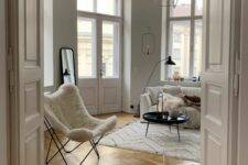 a cozy neutral Scandinavian space with a white sofa and a white faux fur butterfly chair, a pendant lamp, a jar with pillar candles