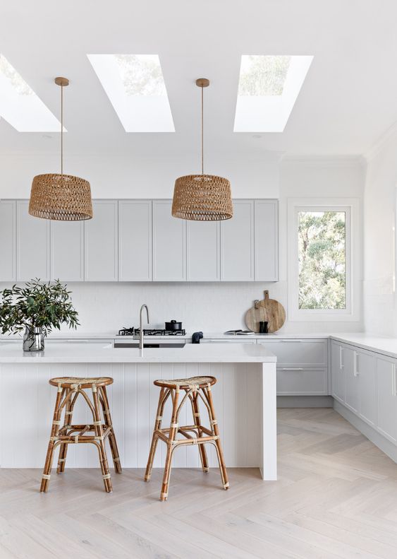 a dove grey kitchen with white countertops, a white backsplash, a white kitchen island, rattan stools and woven pendant lamps