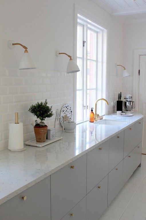 a dove grey kitchen with white stone countertops, a white tile backsplash, white sconces and gold touches