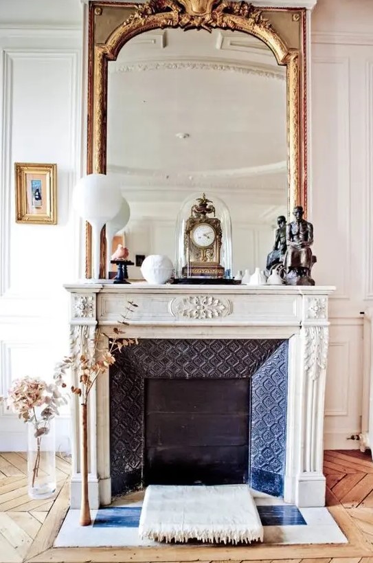 a fabulous French fireplace with an ornated white mantel, an oversized mirror and some vintage decor on the mantel