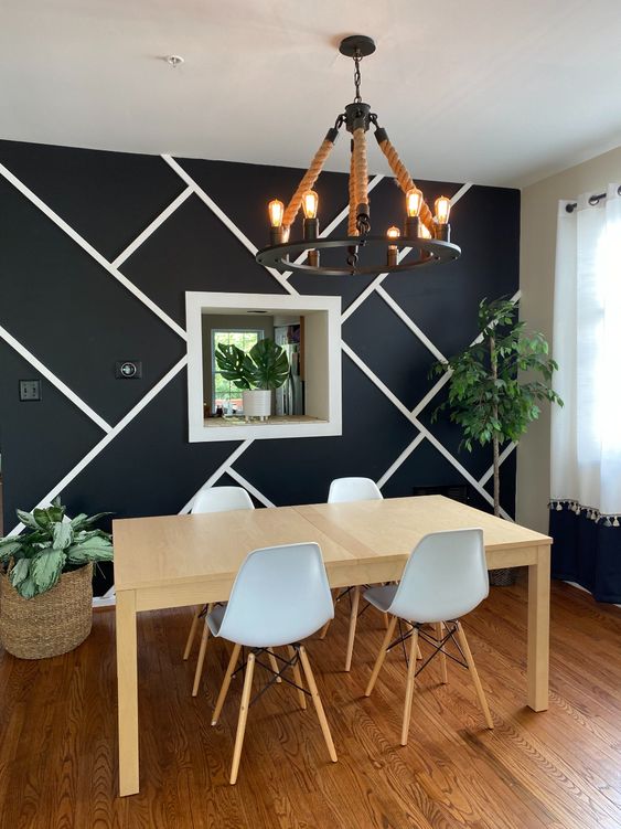 a farmhouse dining room with a black geo accent wall, a stained dining table, a black chandelier, potted plants and a white Eames chairs