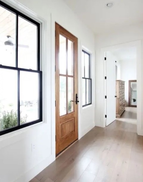 a farmhouse entryway with black double-hung black frame windows, a stained door and white walls with trim