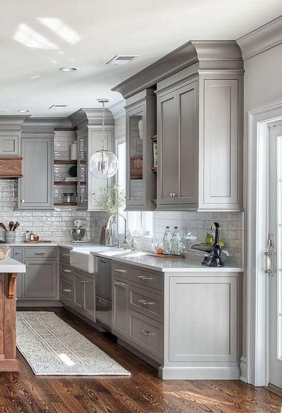 a farmhouse kitchen in dove grey with a white tile backsplash, a bubble lamp and rich stained wood for a warm touch