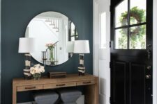 a glam art deco entryway with a wooden console table, grey stools, printed base lamps and a round mirror