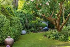 a gorgeous small garden with a green lawn, shrubs and blooming trees, pots and flowers is a cool and fairy-tale like space