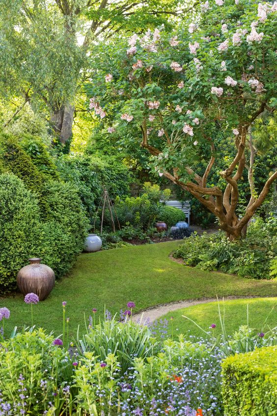a gorgeous small garden with a green lawn, shrubs and blooming trees, pots and flowers is a cool and fairy tale like space
