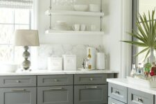 a grey and white farmhouse kitchen with shaker cabinets and white suspended shelves, a white marble backsplash and countertops