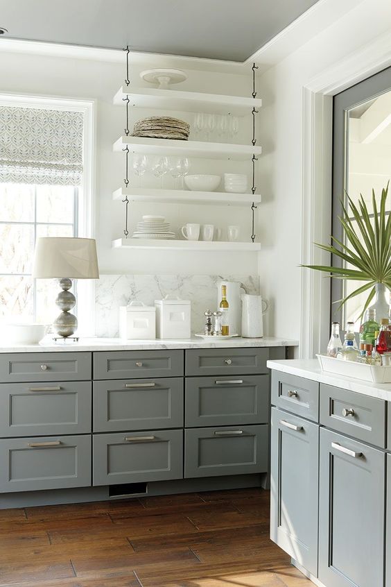 a grey and white farmhouse kitchen with shaker cabinets and white suspended shelves, a white marble backsplash and countertops