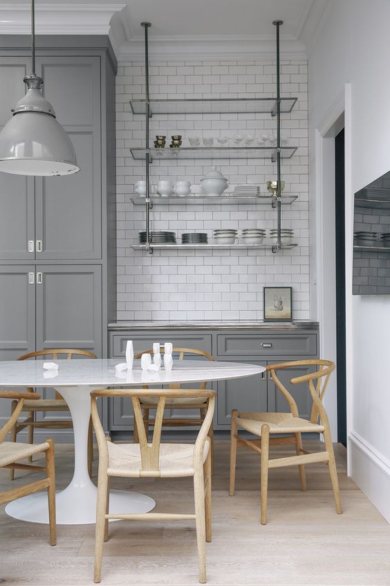 a grey farmhouse kitchen with a white subway tile backsplash, a suspended glass shelf, an oval table and stained chairs