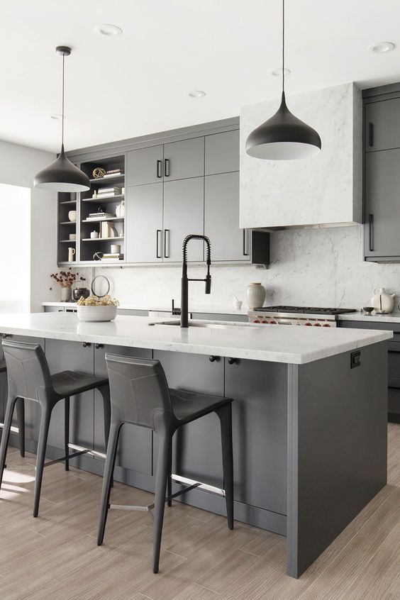 a grey farmhouse kitchen with white countertops, a white marble backsplash, black pendant lamps and black stools