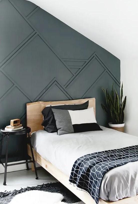 a guest bedroom with a graphite grey paneled wall, a wooden bed, graphic bedding and a statement plant in the corner