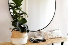 a large round mirror in a black frame and a wooden bench for a simple boho chic space