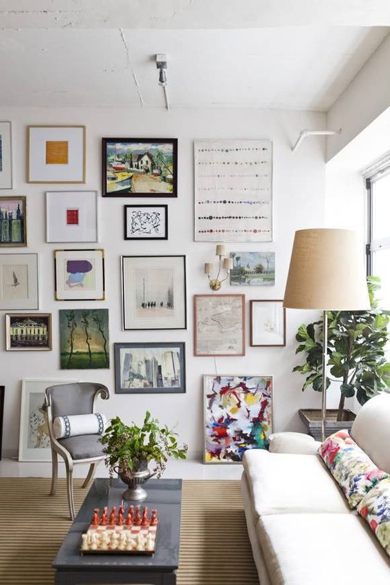 a light-filled living room with a floor to ceiling gallery wall, a creamy sofa with colorful pillows, a chess table and potted plants