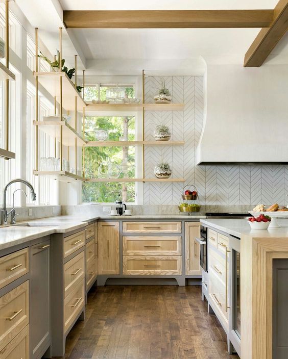 a light-stained farmhouse kitchen with shaker cabinets, a large hood, suspended shelves and a kitchen island