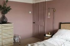 a lovely bedroom with mauve walls, a rattan bed, a wooden sideboard, neutral bedding and touches of gold