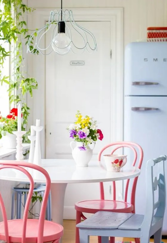 a lovely dining nook with a round table, pink and a pale blue chair, a pale blue Smeg fridge and a pendant lamp with a blue wire lampshade