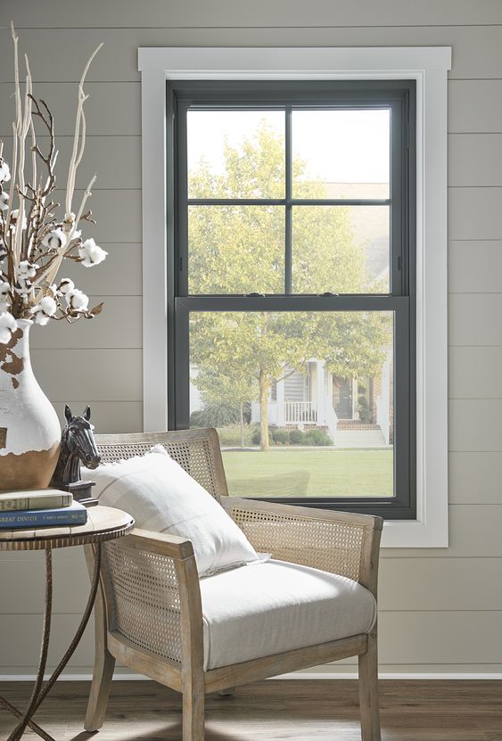 a lovely nook with a double-hung window, a neutral rattan chair, a side table and dried blooms in a color block vase