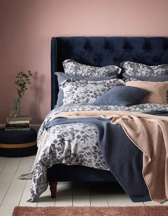 a mauve bedroom with a navy velvet bed, blue and tan bedding with a floral print, a navy ottoman