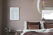 a mauve bedroom with simple furniture, layered bedding, an artwork, a rattan lamp and some blooms is very soothing