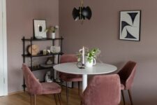 a mauve dining room with a white round table, pink chairs, a black shelving unit and a black pendant lamp