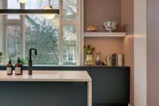 a mauve kitchen with graphite grey cabinets, white and black countertops, pendant lamps and a large window