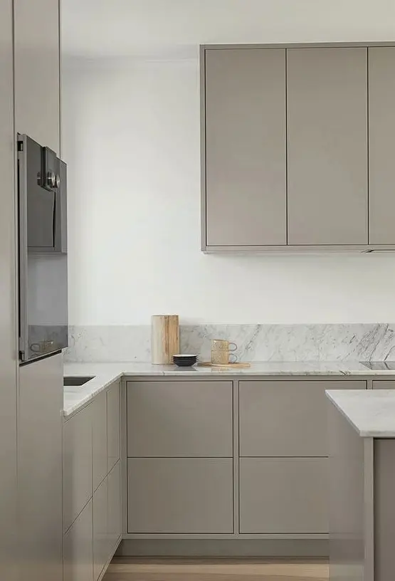 a minimalist Scandinavian kitchen with plain grey cabinets, white marble countertops and a backsplash is airy and serene