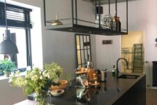 a minimalist kitchen with a black kitchen island and a black suspended shelf over it, with greenery and suspended lamps