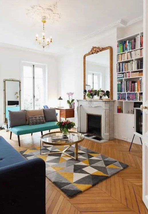 a modern and chic French living room with a French marble fireplace, a bold turquoise loveseat and a navy sofa, mirrors and a glass coffee table