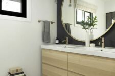 a modern bathroom with a black accent wall, a light-stained vanity, a round mirror, a dark stool and pendant bulbs