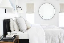 a modern bedroom with a black bed, neutral bedding, a printed rug, a black nightstand and a round mirror