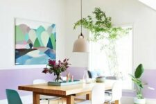 a modern dining room with color block lilac and white walls, a stained dining table, white and blue chairs, potted plants and a bold artwork