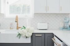 a modern farmhouse kitchen with white upper cabinets and lower grey ones, gold and brass handles plus a white fish scale backsplash