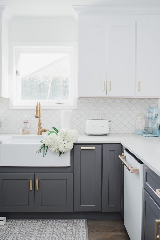 a modern farmhouse kitchen with white upper cabinets and lower grey ones, gold and brass handles plus a white fish scale backsplash