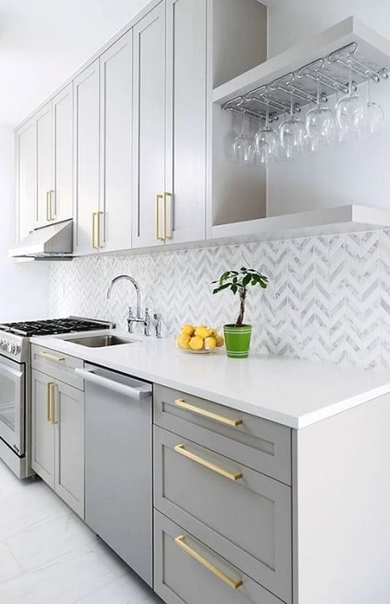 a modern kitchen with dove grey cabinets, a chevron tile backsplash and gold handles looks very chic and elegant