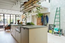 a modern light-stained plywood kitchen with suspended shelves, a skylight and lots of greenery