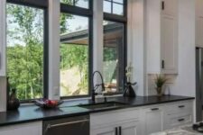 a monochromatic kitchen with shaker cabinets, black and grey stone countertops, black double-hung windows and built-in lights