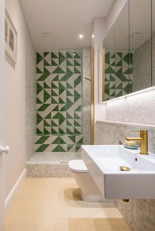a neutral bathroom with small scale tiles, a green and white tile wall in the shower space, white applainces and brass touches